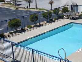 Una piscina con valla azul, un trampolín y un patio con mobiliario exterior.