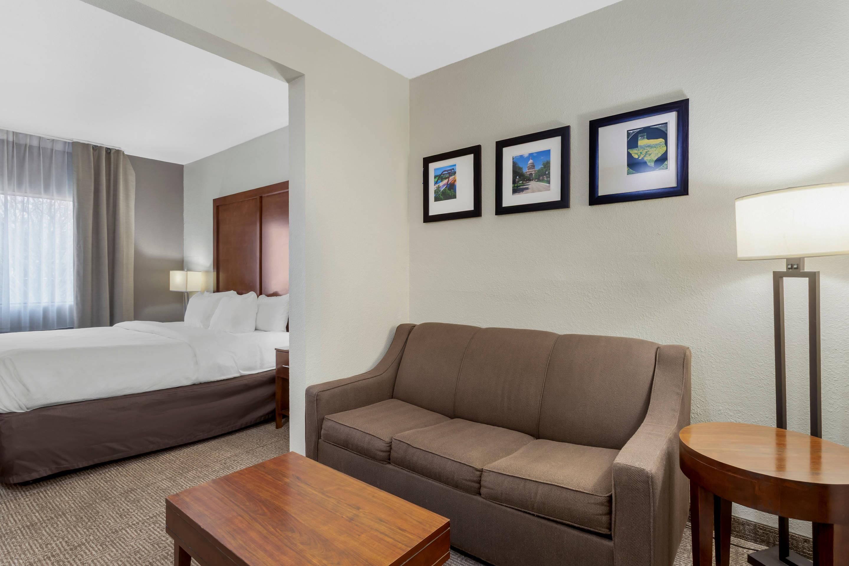 A hotel room with a bed, a sofa, a small table, and three framed pictures on the wall.
