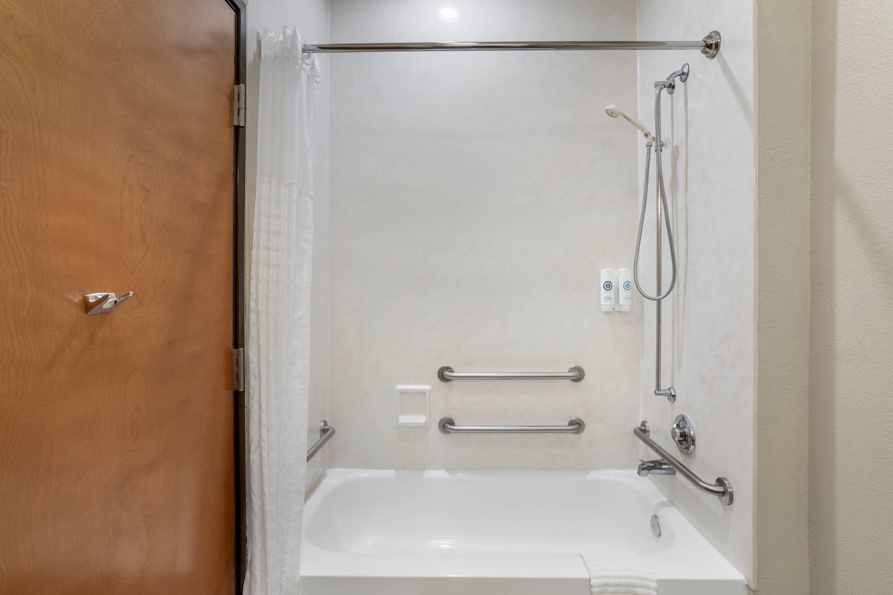 Un baño con bañera, ducha y barras de apoyo.