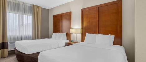 A hotel room with two beds, a nightstand, a lamp, and a window with curtains.