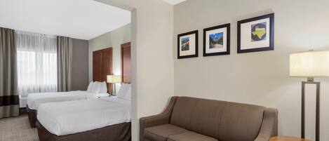 A hotel room with two beds, a sofa, a small table, a lamp, and framed pictures on the wall.