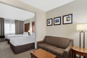 A hotel room with two beds, a sofa, a small table, a lamp, and framed pictures on the wall. - Comfort Suites Brenham (Brenham)