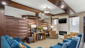 A modern living room with a blue sofa set, a wooden accent wall, a fireplace, and a flat-screen TV mounted on the wall. - Comfort Suites Brenham (Brenham)