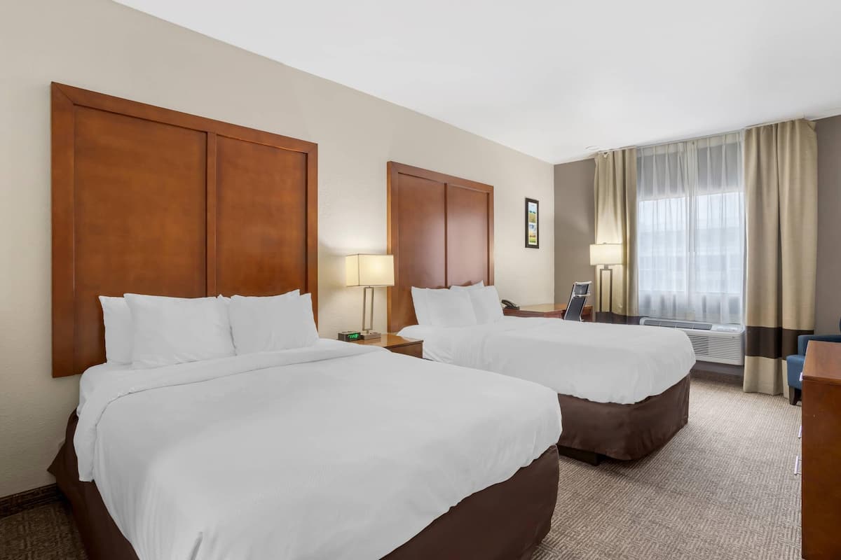 Habitación de hotel con dos camas, un escritorio, una silla, una lámpara y una ventana con cortinas.