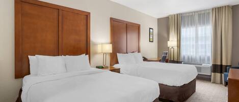Habitación de hotel con dos camas, un escritorio, una silla, una lámpara y una ventana con cortinas.