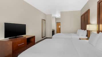 Habitación de hotel con televisión sobre un mueble de madera, dos camas con ropa blanca, una mesita de noche de madera con lámpara y un espejo en la pared.