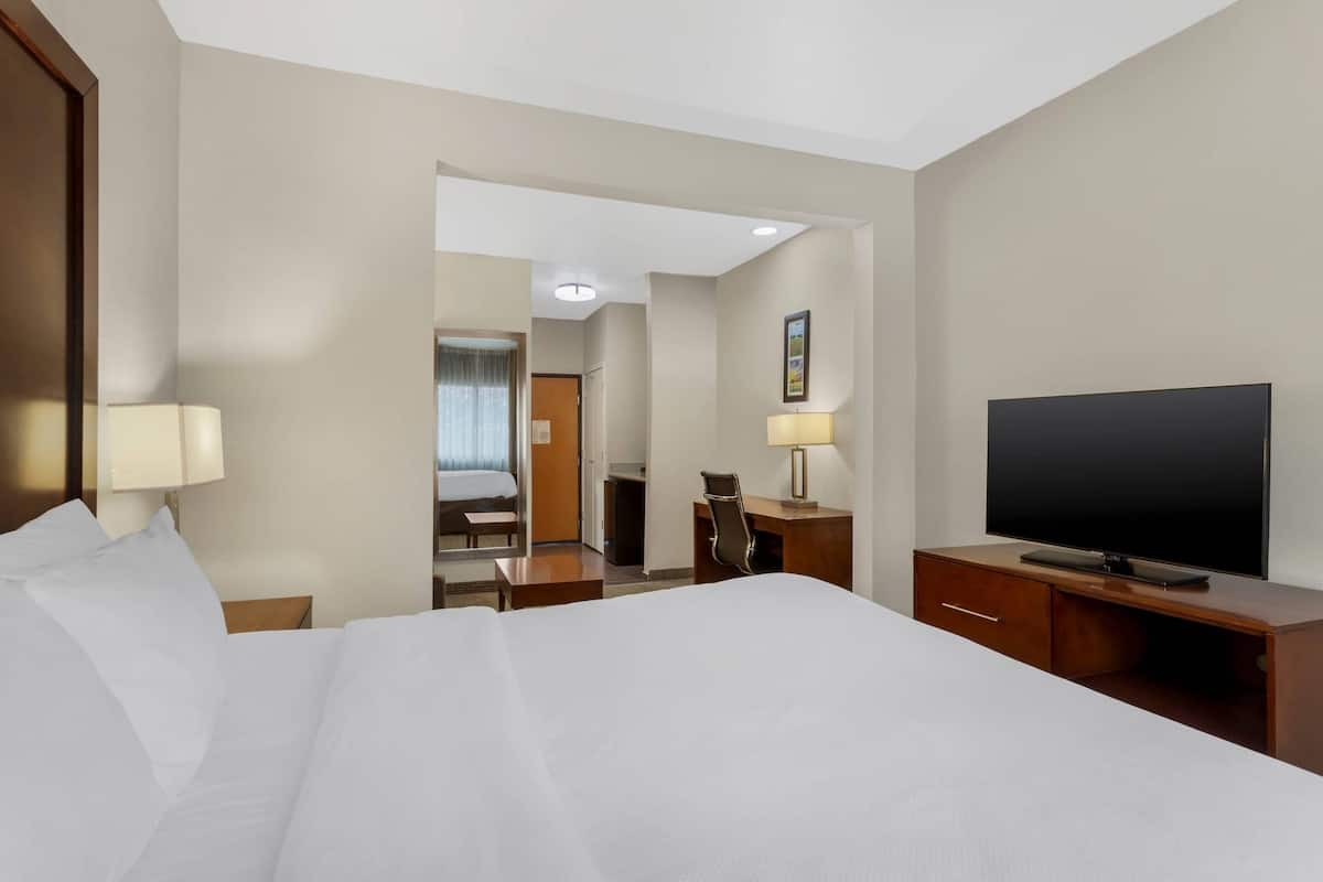 Una habitación de hotel con una cama grande, un escritorio con lámpara, un televisor y un espejo.