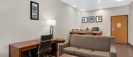 A hotel room with a desk, chair, sofa, and a dining table with chairs.