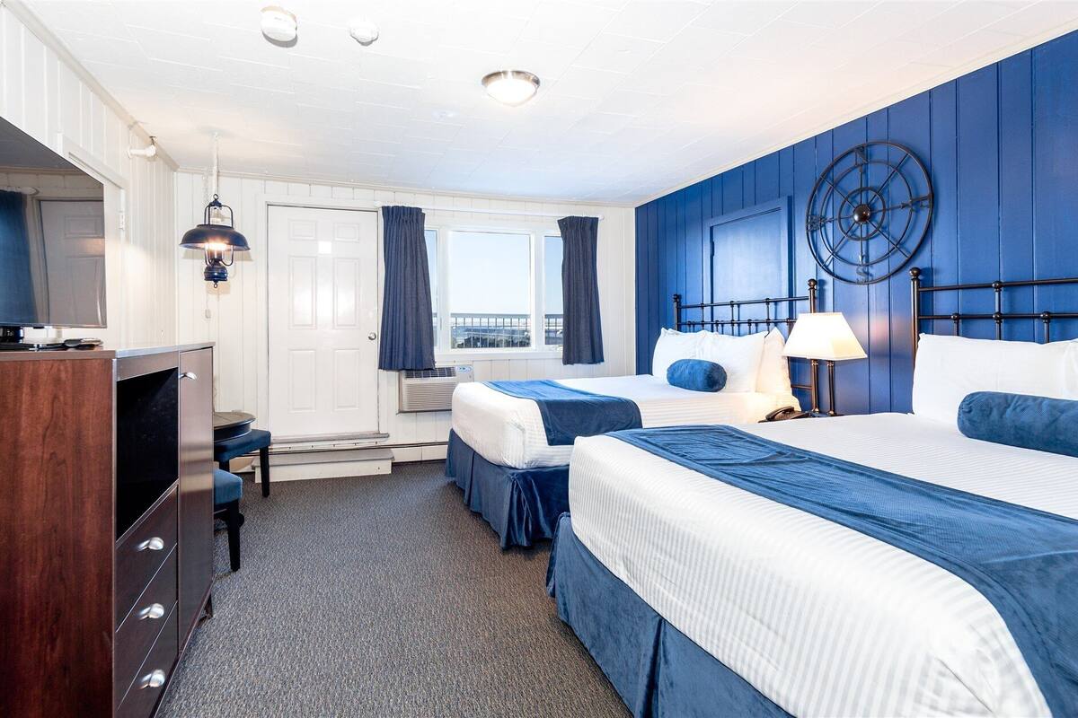 Une chambre d’hôtel avec deux lits, un bureau, une télévision et une fenêtre avec des rideaux.