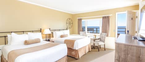 A hotel room with two beds, a desk, a chair, and a view of the sea.