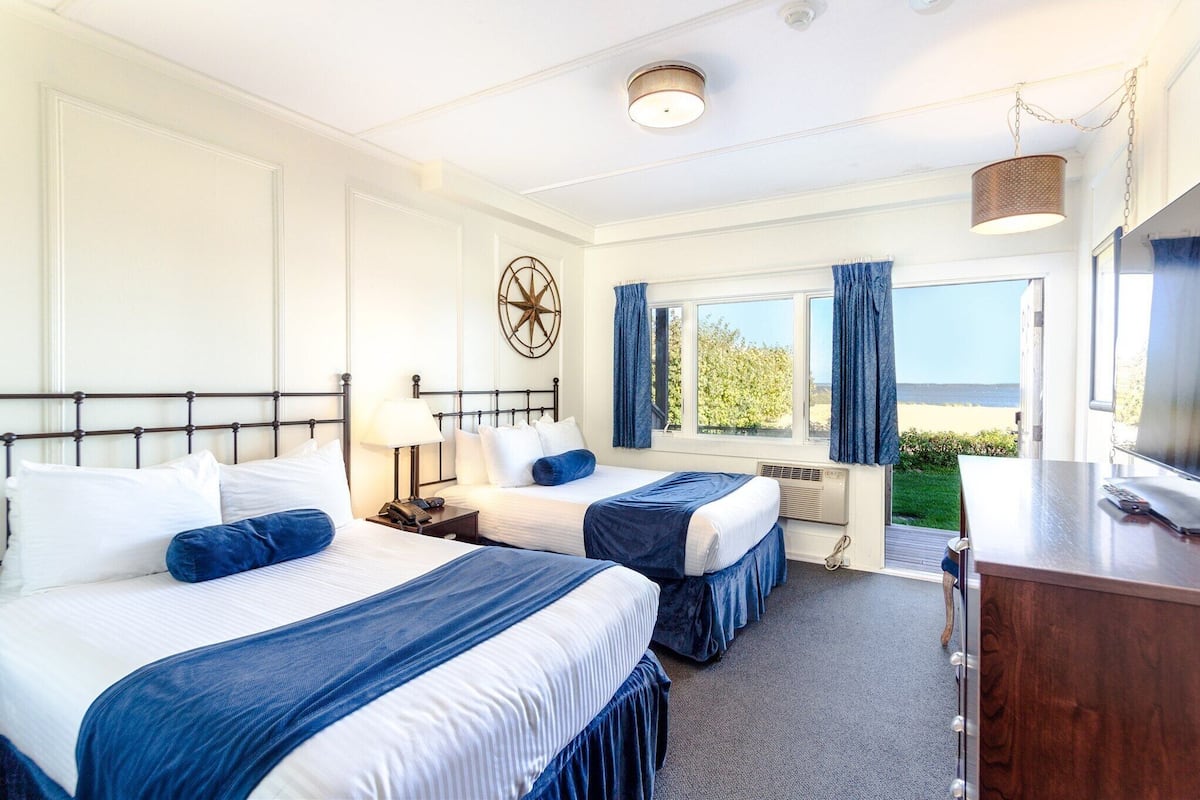 Une chambre d’hôtel avec deux lits, un bureau, une télévision et une fenêtre avec des rideaux.