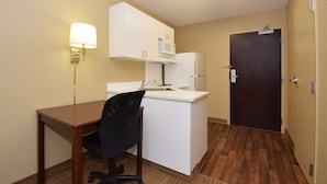 A compact kitchen with a microwave, refrigerator, and a small sink. There is a wooden desk and a black office chair. A door is visible in the background. - Extended Stay America Suites Seattle Northgate (Seattle)