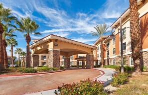 A hotel entrance with a covered walkway, palm trees, and a clear sky.