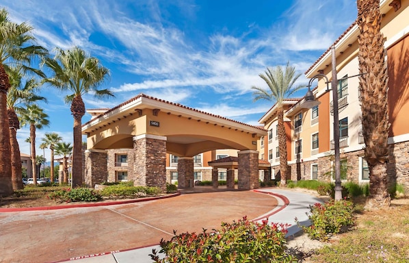 A hotel entrance with a covered walkway, palm trees, and a clear sky.