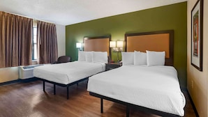 Habitación de hotel con dos camas, una silla, un escritorio con lámpara y un cuadro en la pared.