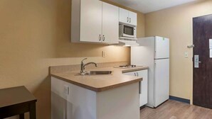 Una cocina compacta con armarios blancos, un microondas, un refrigerador y un lavamanos.