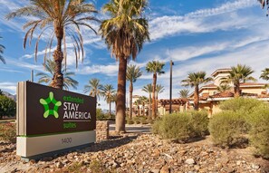 A sign for Extended Stay America Suites with a desert landscape and palm trees in the background.