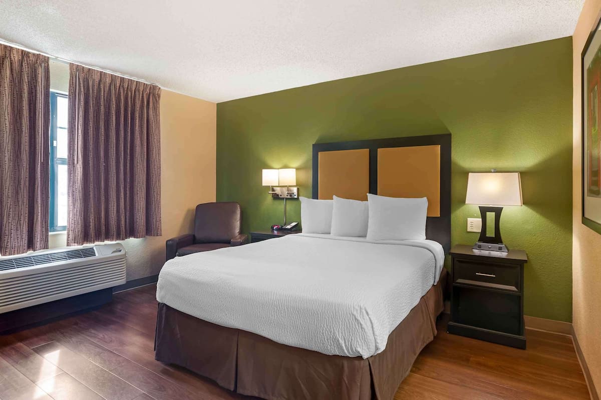 A hotel room with a large bed, two bedside tables with lamps, a chair, and a window with curtains.