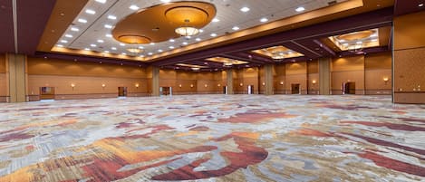 Un amplio salón de conferencias con alfombra estampada, iluminación empotrada y un techo alto.