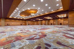 Un amplio salón de conferencias con alfombra estampada, iluminación empotrada y un techo alto.
