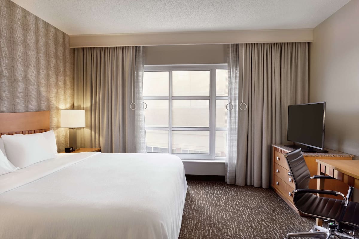 Een hotelkamer met een groot bed, een bureau met stoel, een televisie en een raam met gordijnen.