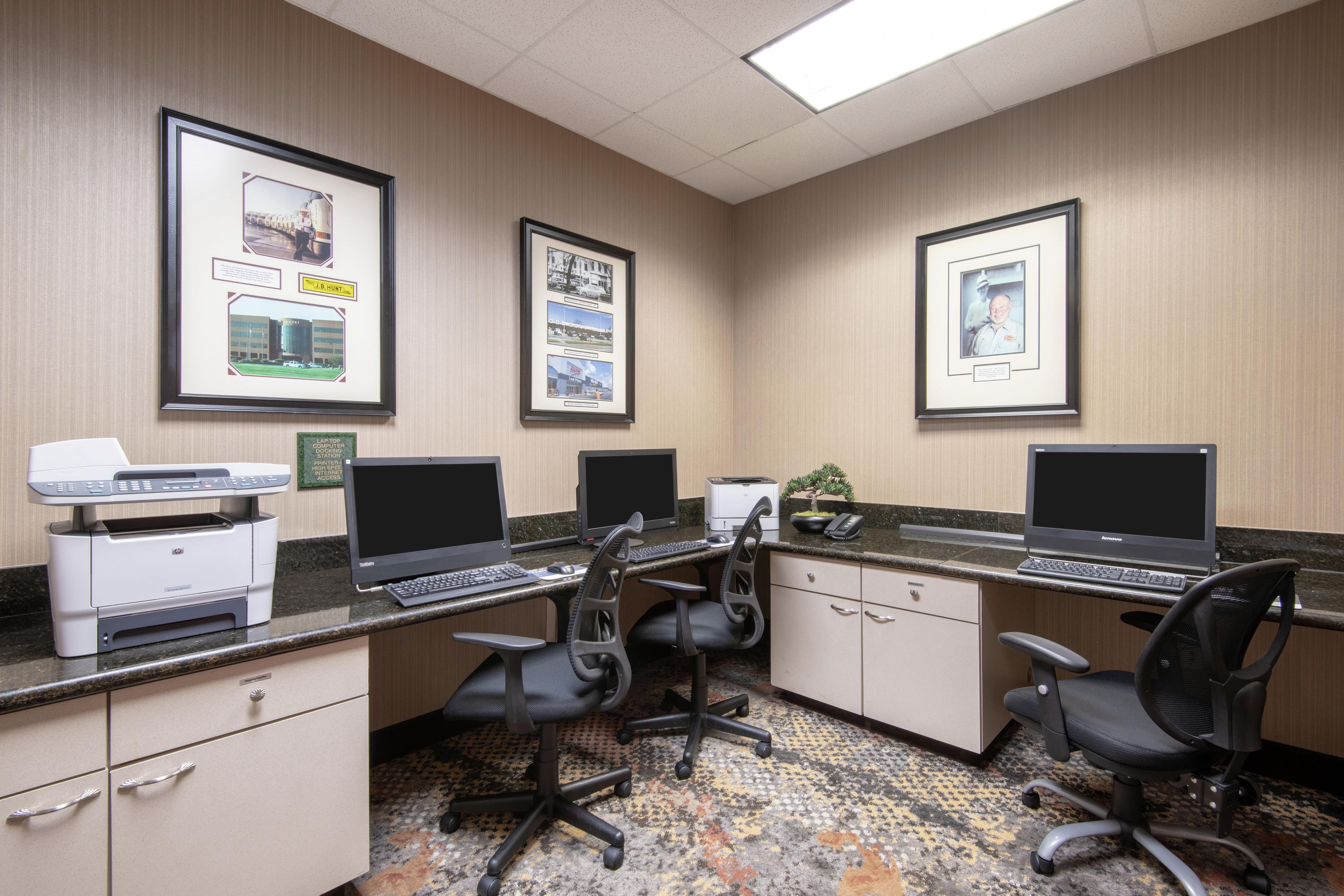 A hotel office with three desks, two printers, and framed pictures on the wall.
