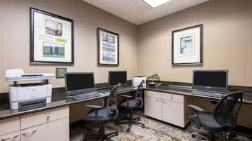 A hotel office with three desks, two printers, and framed pictures on the wall.