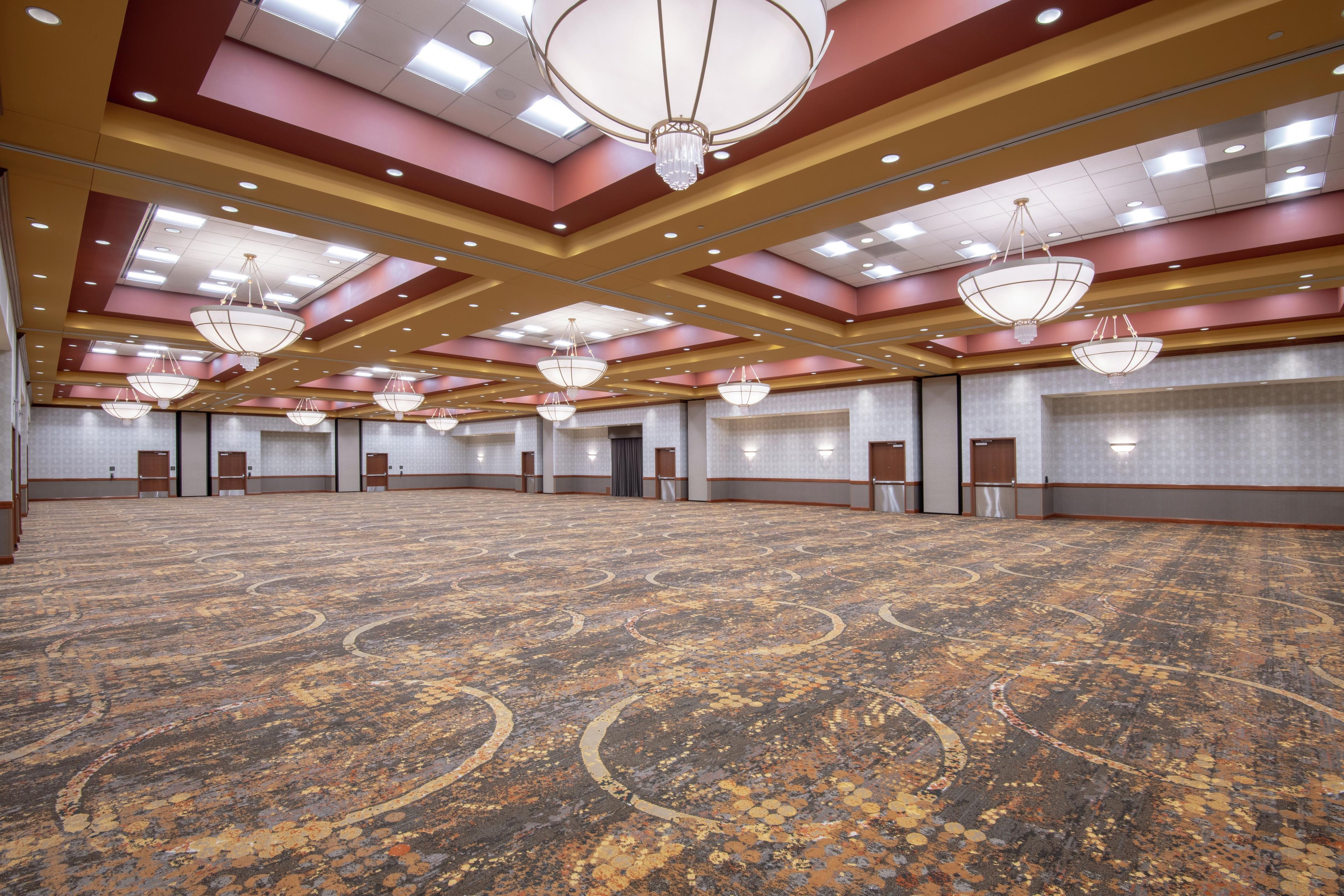 Un salón de conferencias amplio con alfombra estampada, varias puertas y candelabros en el techo.