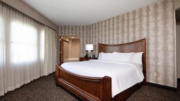 Hotelkamer met een groot bed, een nachtkastje met een lamp, een zichtbare badkamer door een open deur en behang met een patroon.