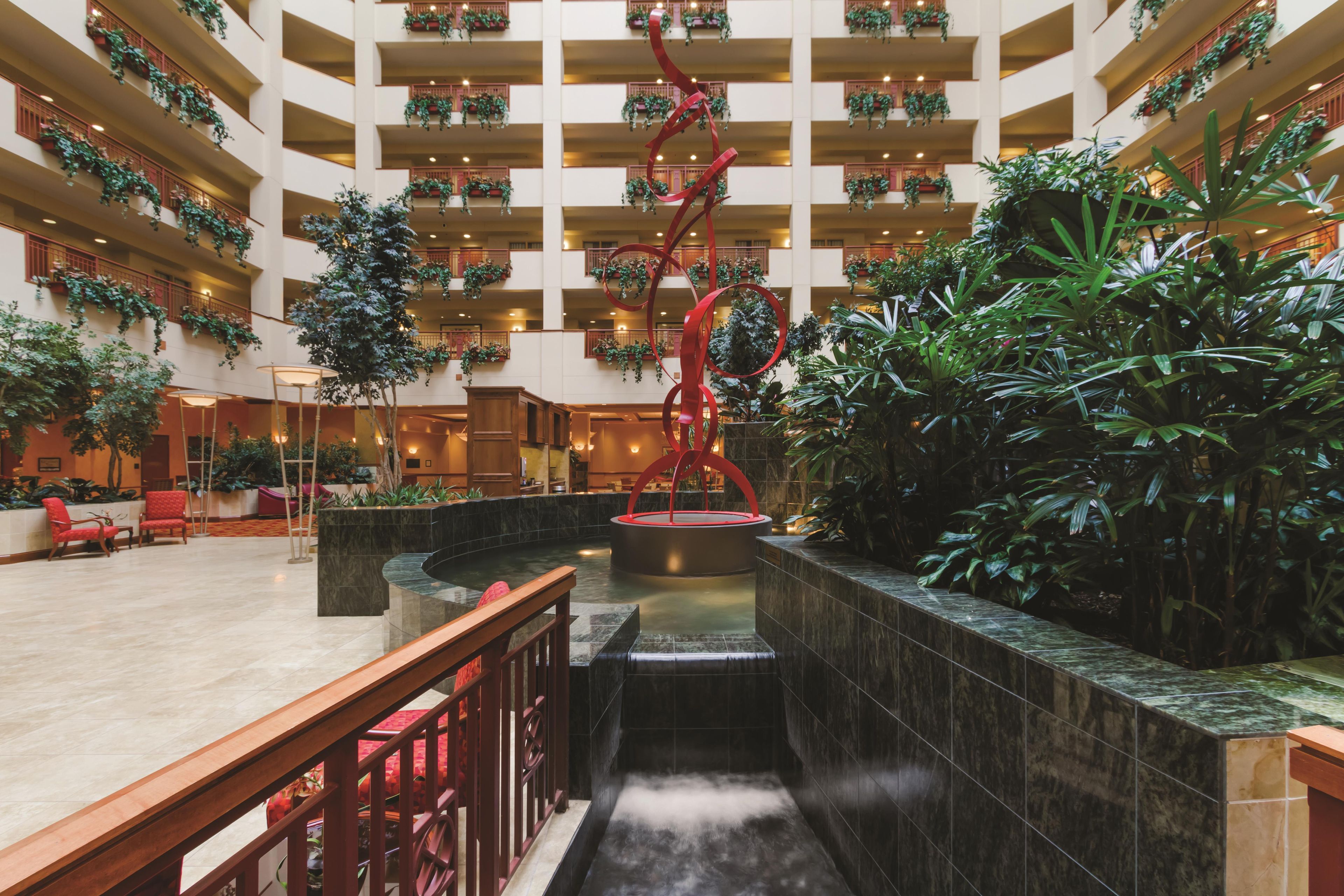 A multi-level atrium with a central water feature, surrounded by lush greenery and red railings.