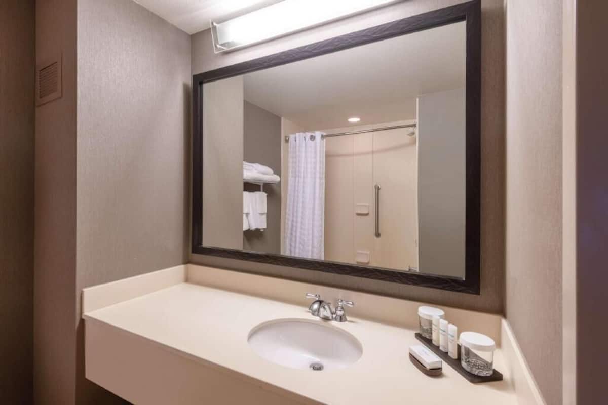 Een badkamer met een grote spiegel, een wastafel en een douchehoek.