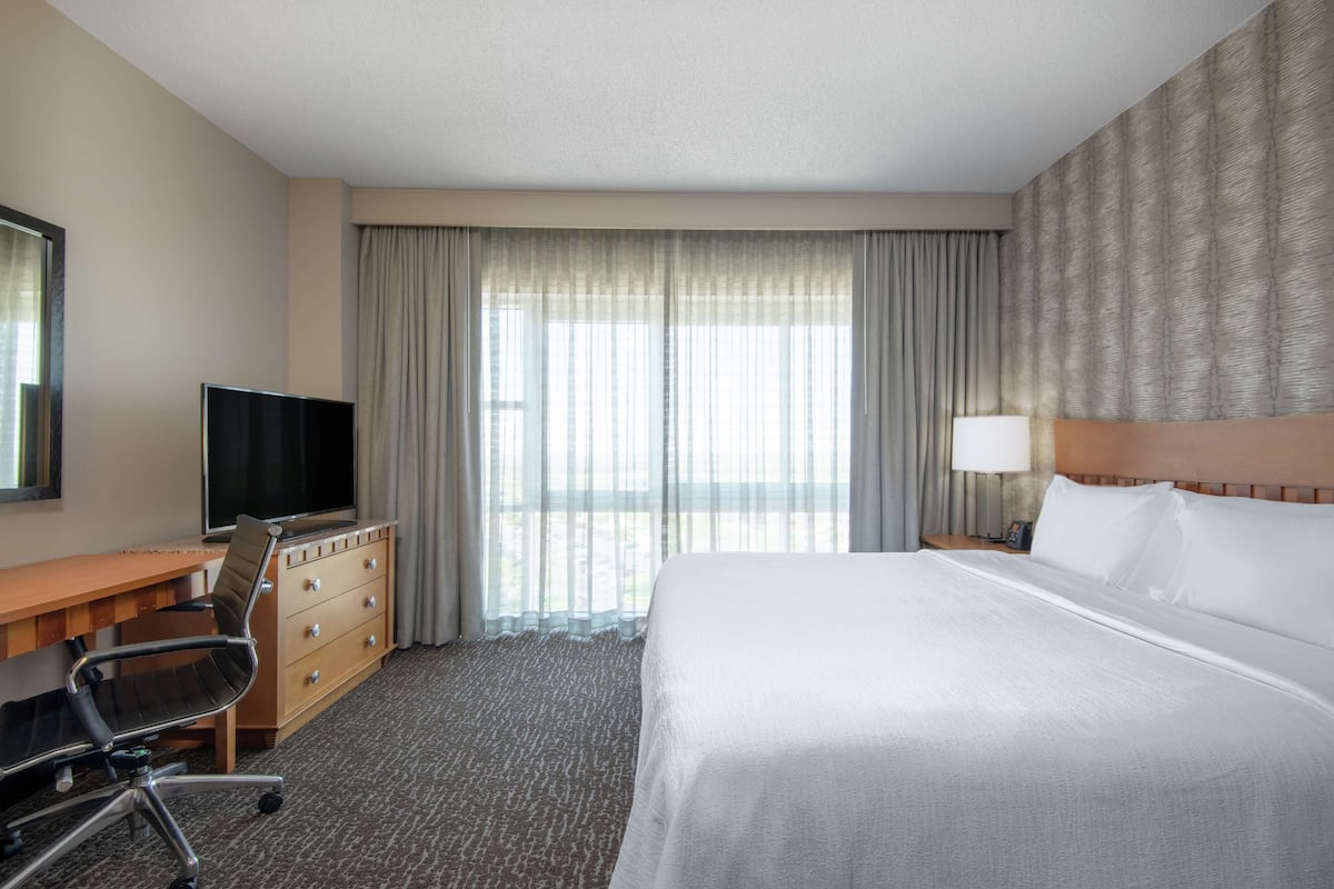 Een hotelkamer met een bed, een bureau met stoel, een televisie en een groot raam met gordijnen.
