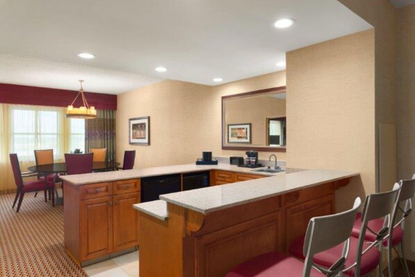 Habitación de hotel con kitchenette, zona de comedor con mesa y sillas, y un espejo grande en la pared.