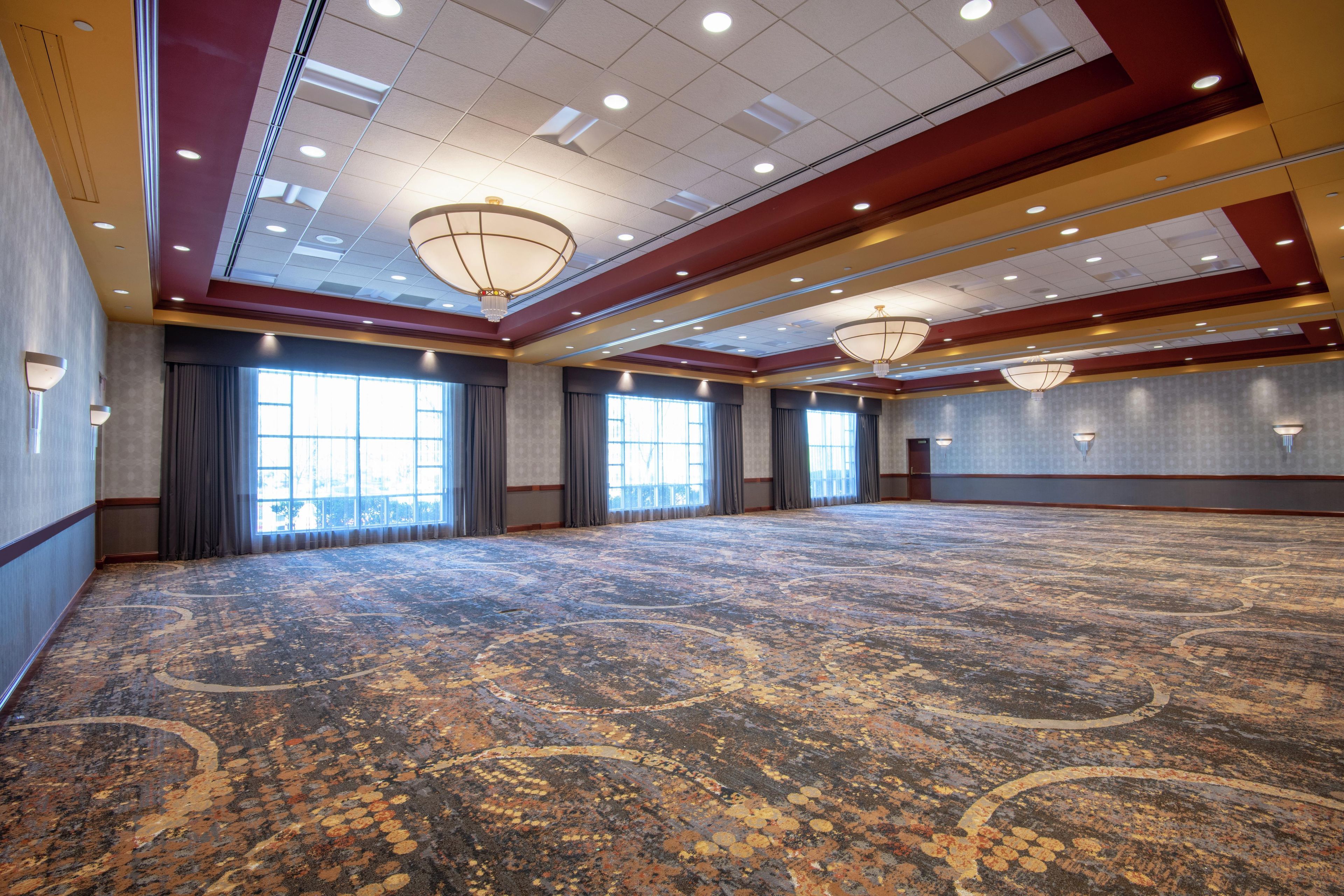 A large conference room with a patterned carpet, multiple windows with curtains, and ceiling lights.
