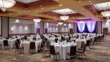 Un salón de banquetes con mesas redondas dispuestas para cenar, candelabros y un escenario con cortinas.