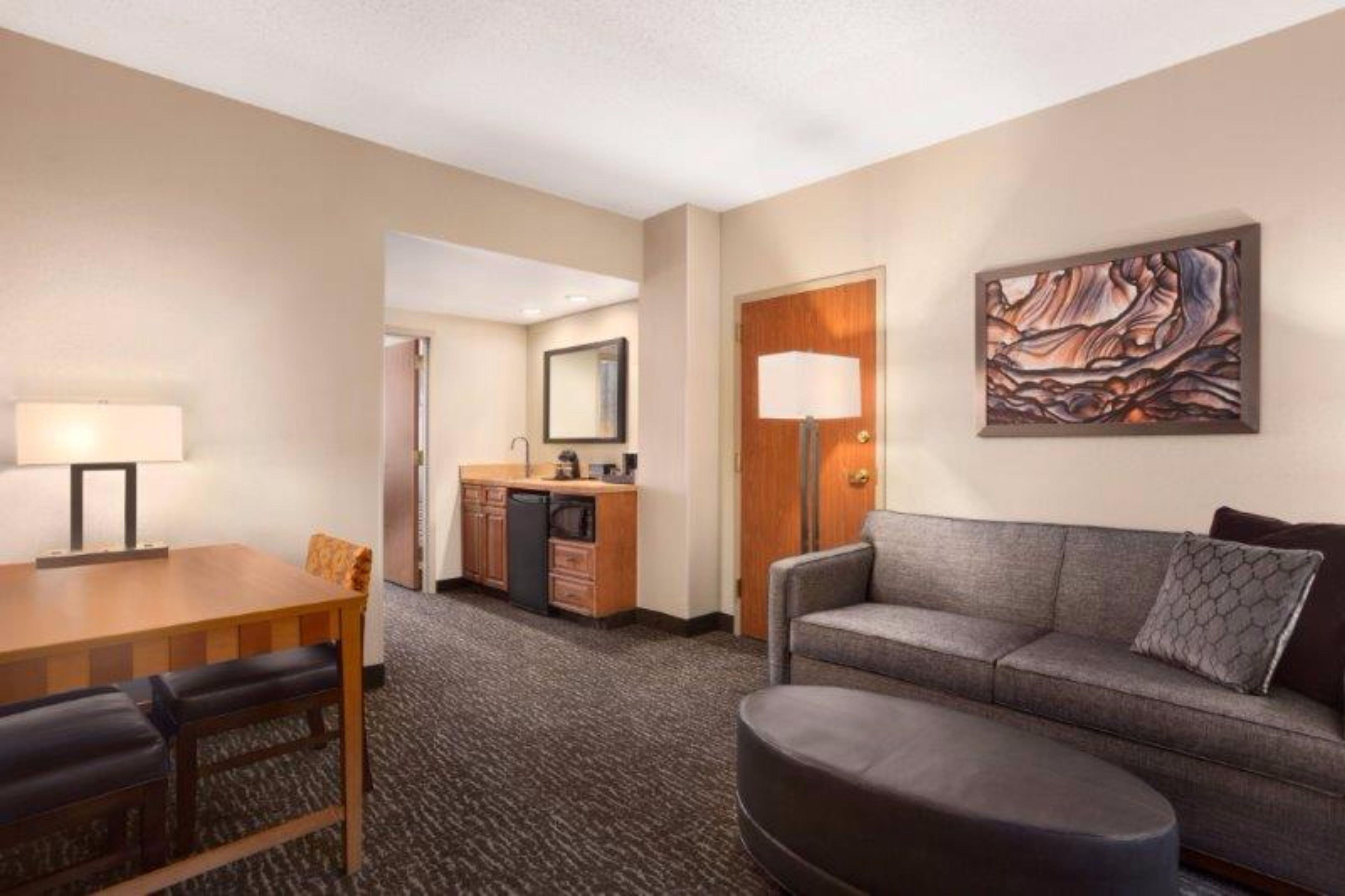 Habitación de hotel con una mesa de comedor, un sofá, una zona de cocina y un cuadro en la pared.