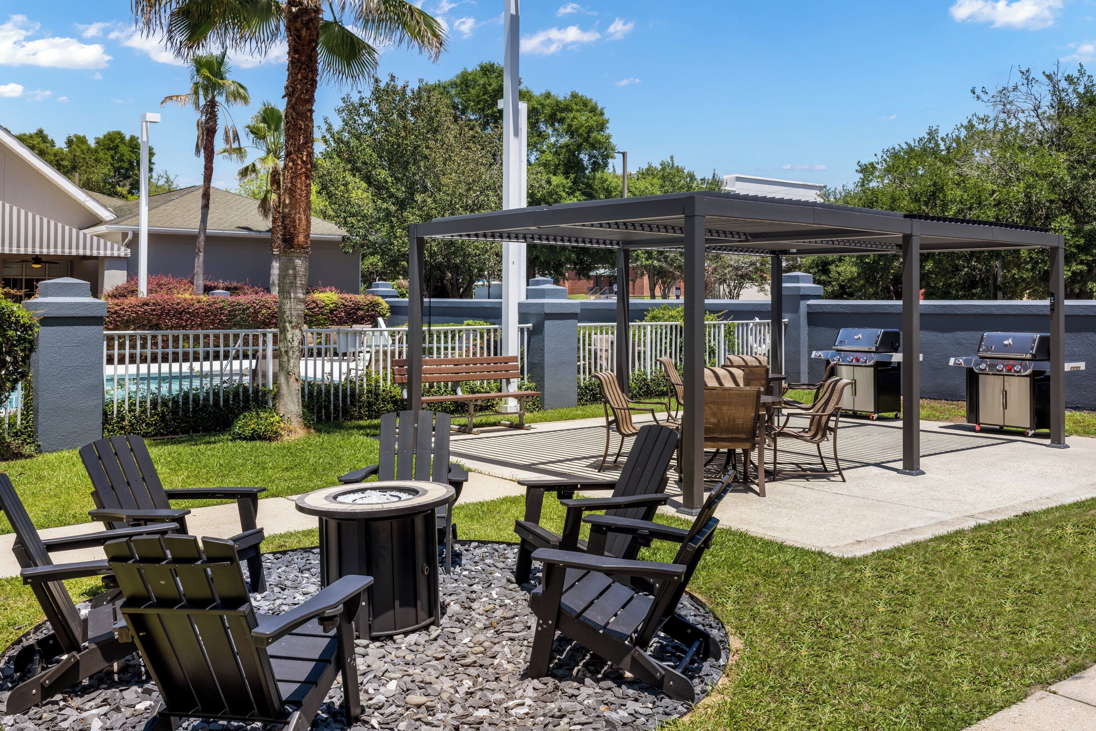 An outdoor patio area with Adirondack chairs, a fire pit, a covered seating area, and a barbecue grill.