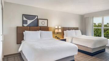 Quarto de hotel com duas camas, uma mesa de cabeceira com luminárias e uma janela grande com vista.