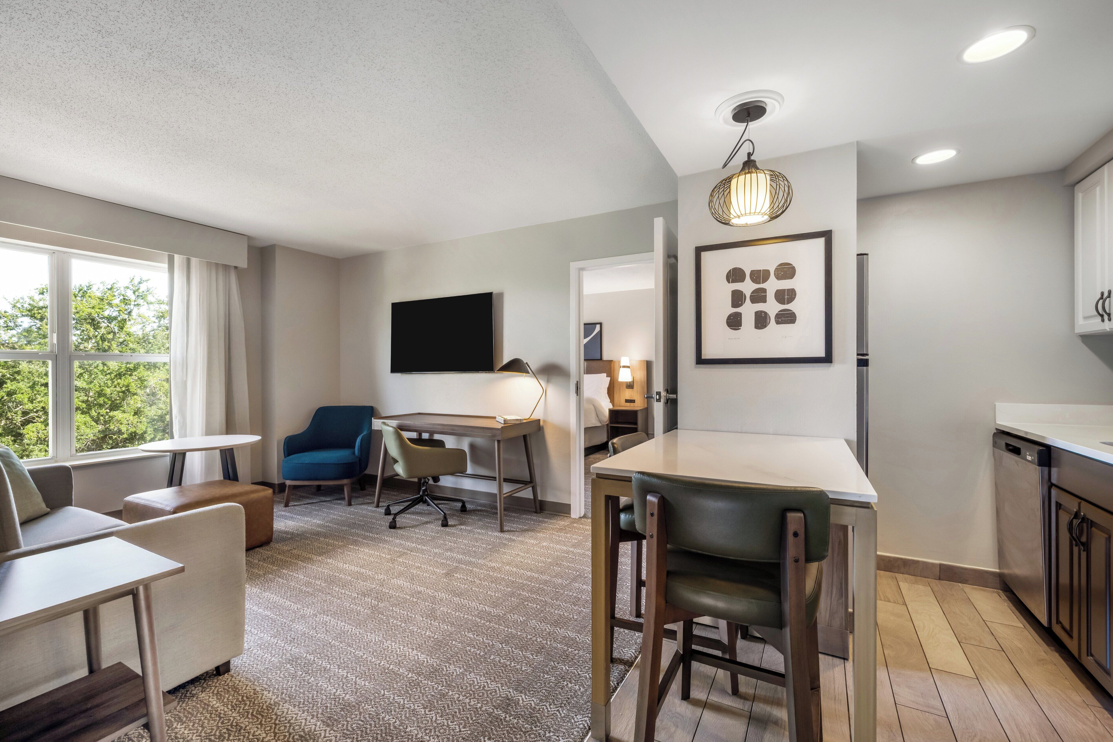 A modern living room with a flat-screen TV, a dining table, and a kitchen area with a dishwasher.