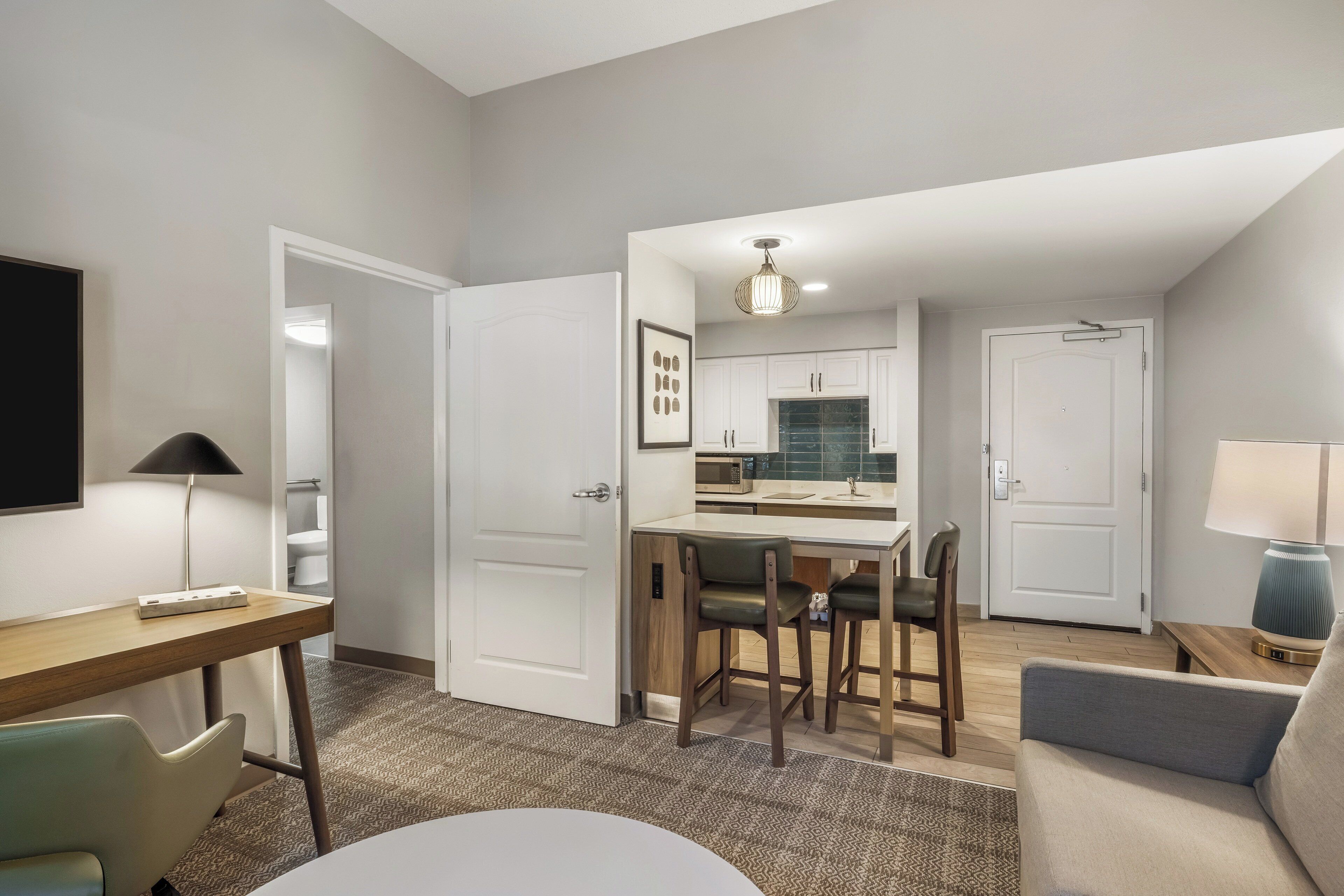 A modern hotel room with a dining area, a sofa, a desk, and a TV.
