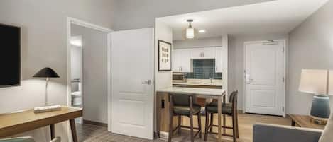 Una habitación de hotel moderna con zona de comedor, sofá, escritorio y televisor.