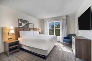 A hotel room with a bed, bedside tables, a chair, a desk, a TV, and a window with curtains. - Staybridge Suites Pensacola Airport by IHG (Pensacola)