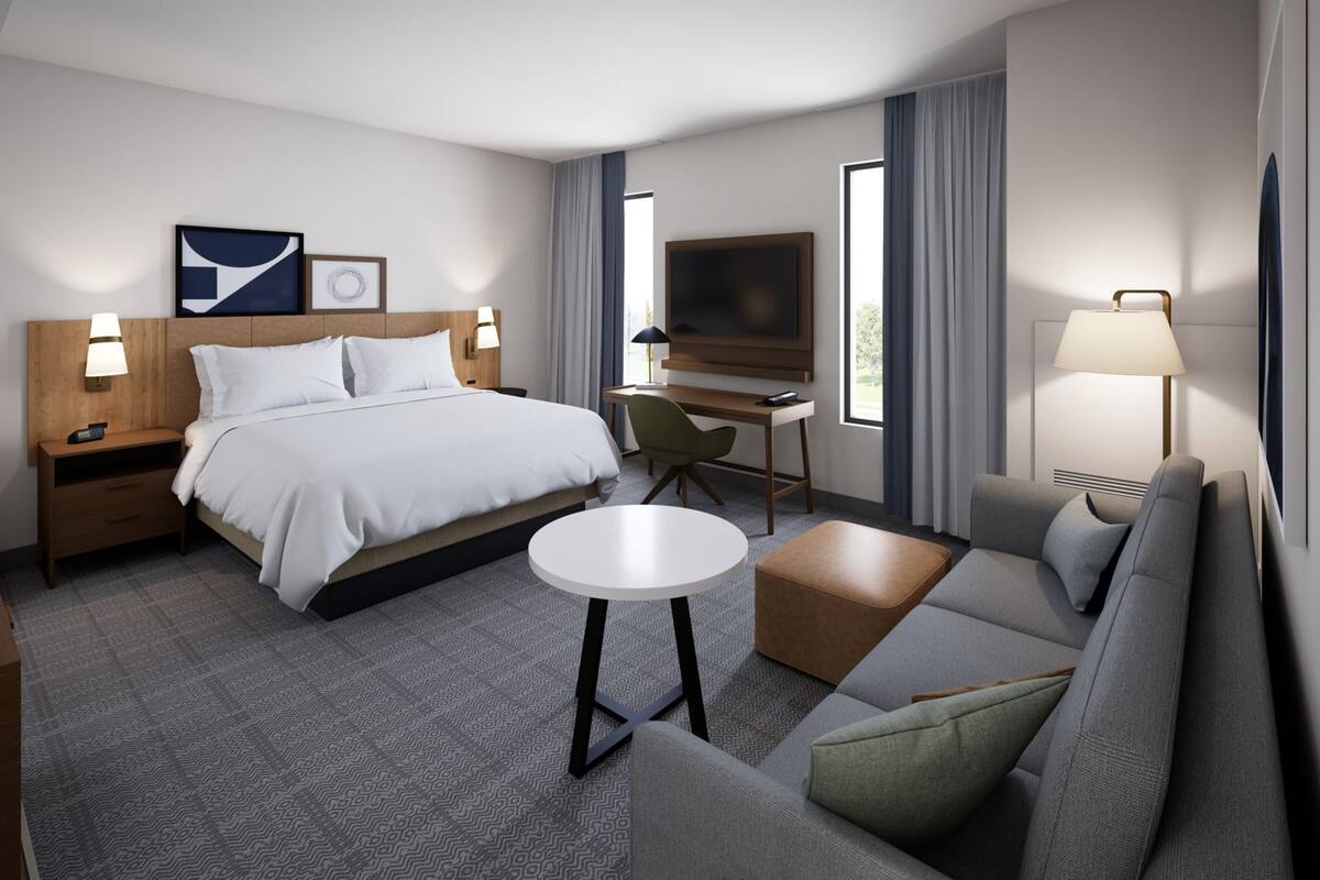 A hotel room with a bed, a desk, a TV, a sofa, and a lamp.