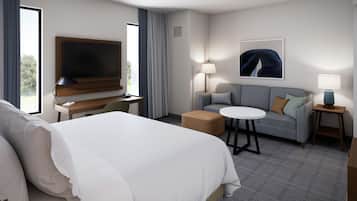 A hotel room with a bed, a desk with a flat-screen TV, a sofa, a small round table, and a lamp.