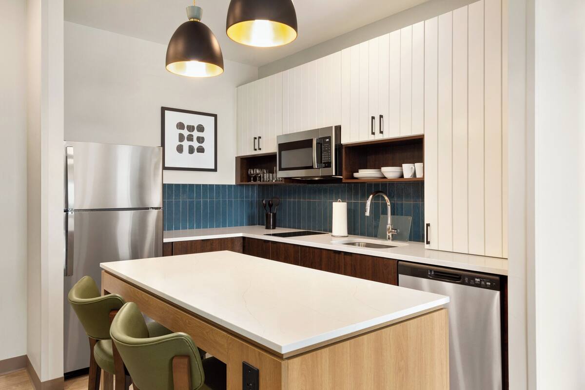 A modern kitchen with a central island, stainless steel appliances, and a blue backsplash.