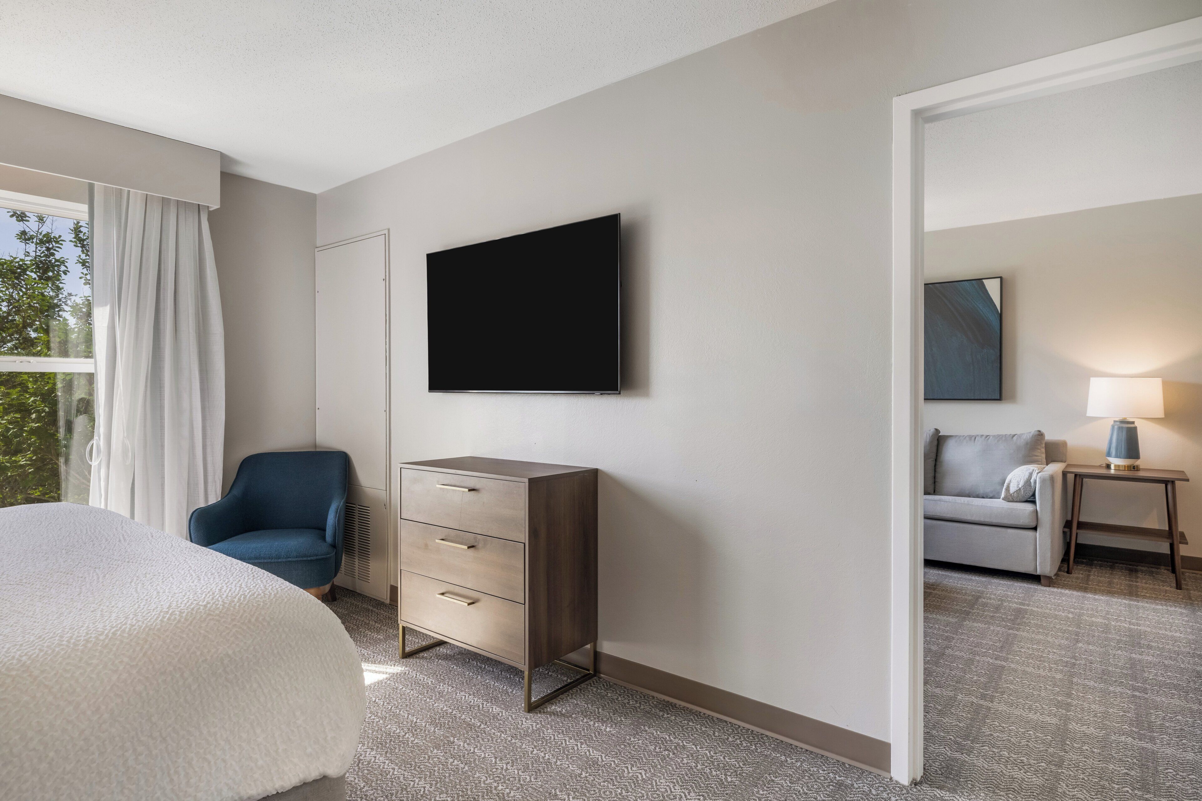 Une chambre d’hôtel comprenant un lit, une commode, une télévision, une chaise, un canapé et une lampe.