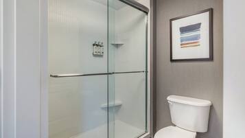 A bathroom with a glass shower enclosure, a white toilet, and a framed abstract painting on the wall.