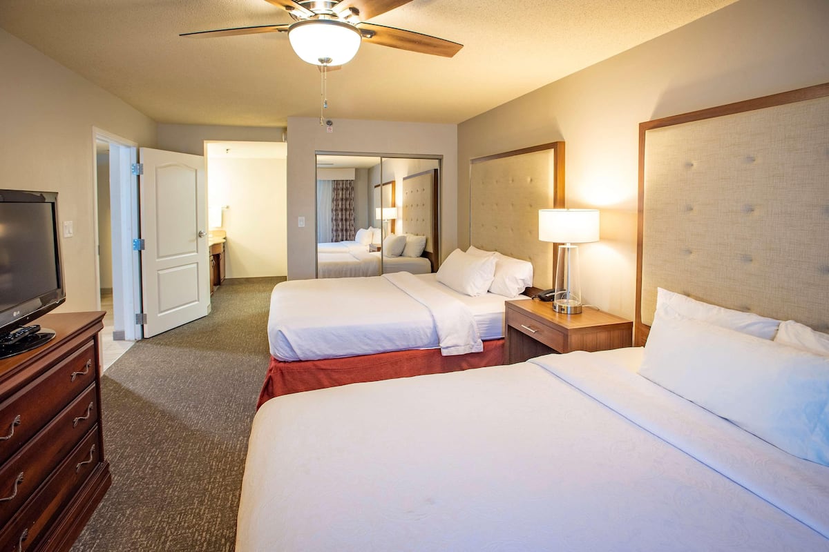 A hotel room with two beds, a ceiling fan, a TV, and a dresser.