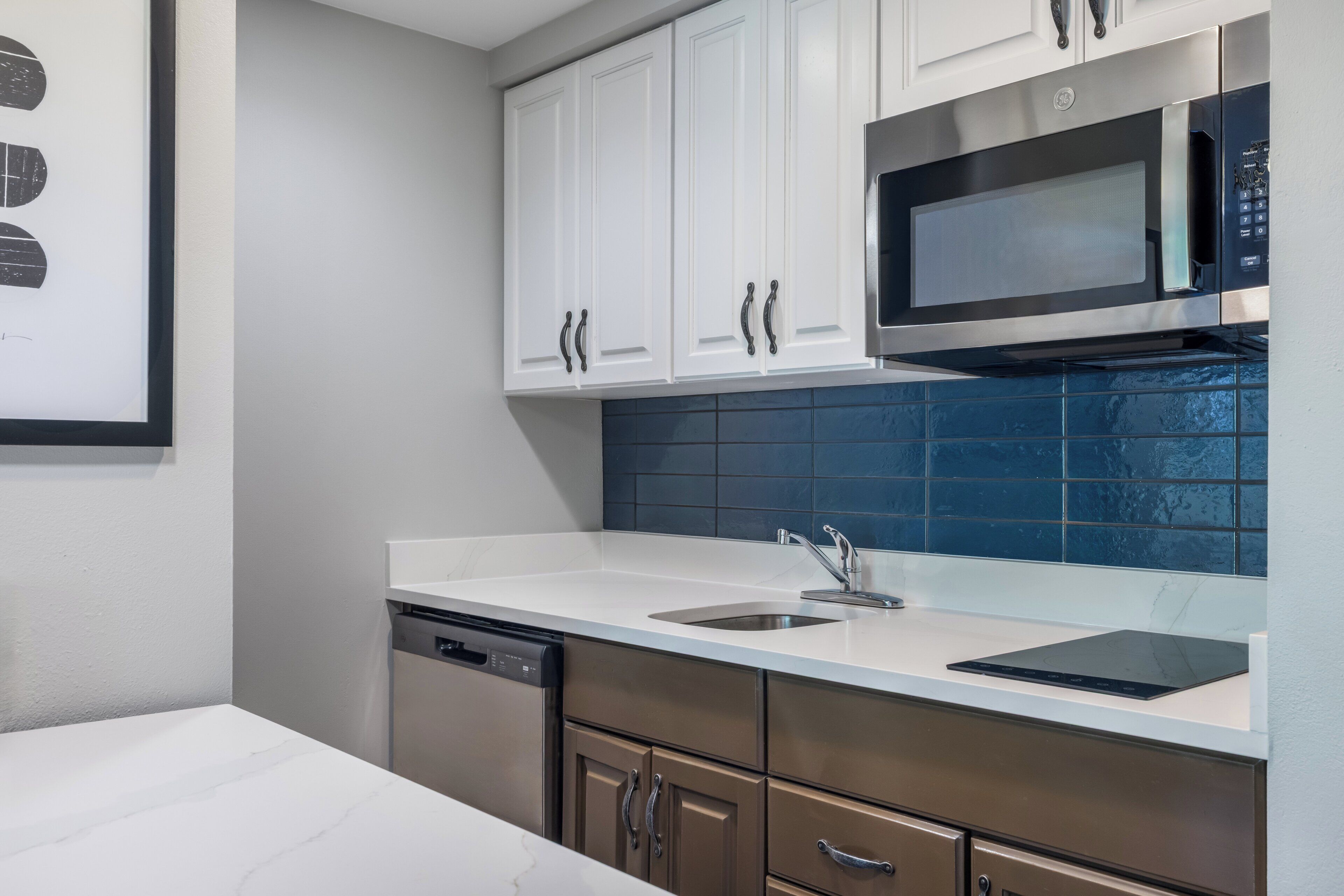 A kitchen with white cabinets, a stainless steel microwave, a dishwasher, and a blue tiled backsplash.