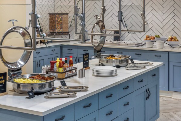Buffet com diversos alimentos, utensílios e acompanhamentos.